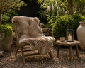 Wooden chair with fur cover in a garden setting with a small table and lantern. - Leading Landscapes Canterbury