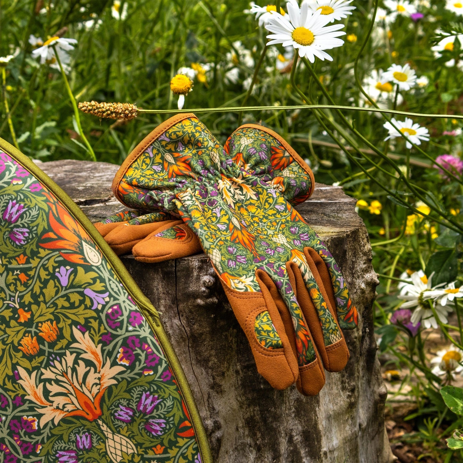 Pair of patterned gardening gloves on a wooden stump with flowers in the background