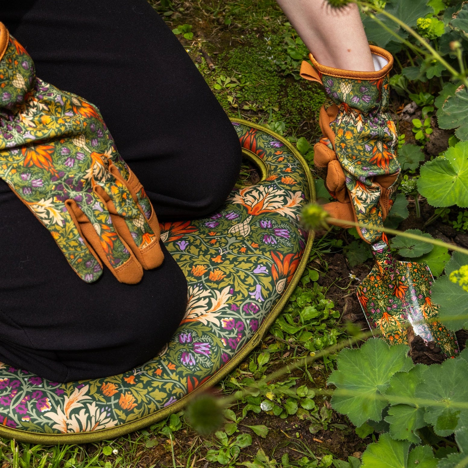 Person wearing floral gardening gloves and a matching kneeling pad in a garden setting.