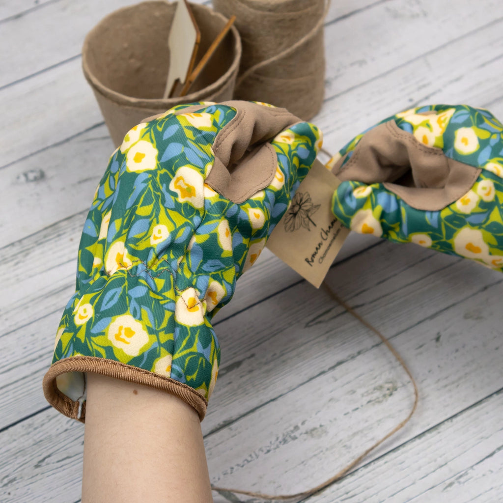 Pair of floral-patterned gardening gloves on a wooden surface with a small pot and twine in the background.