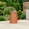 Copper watering can on a patio with greenery in the background - Leading Landscapes Limited
